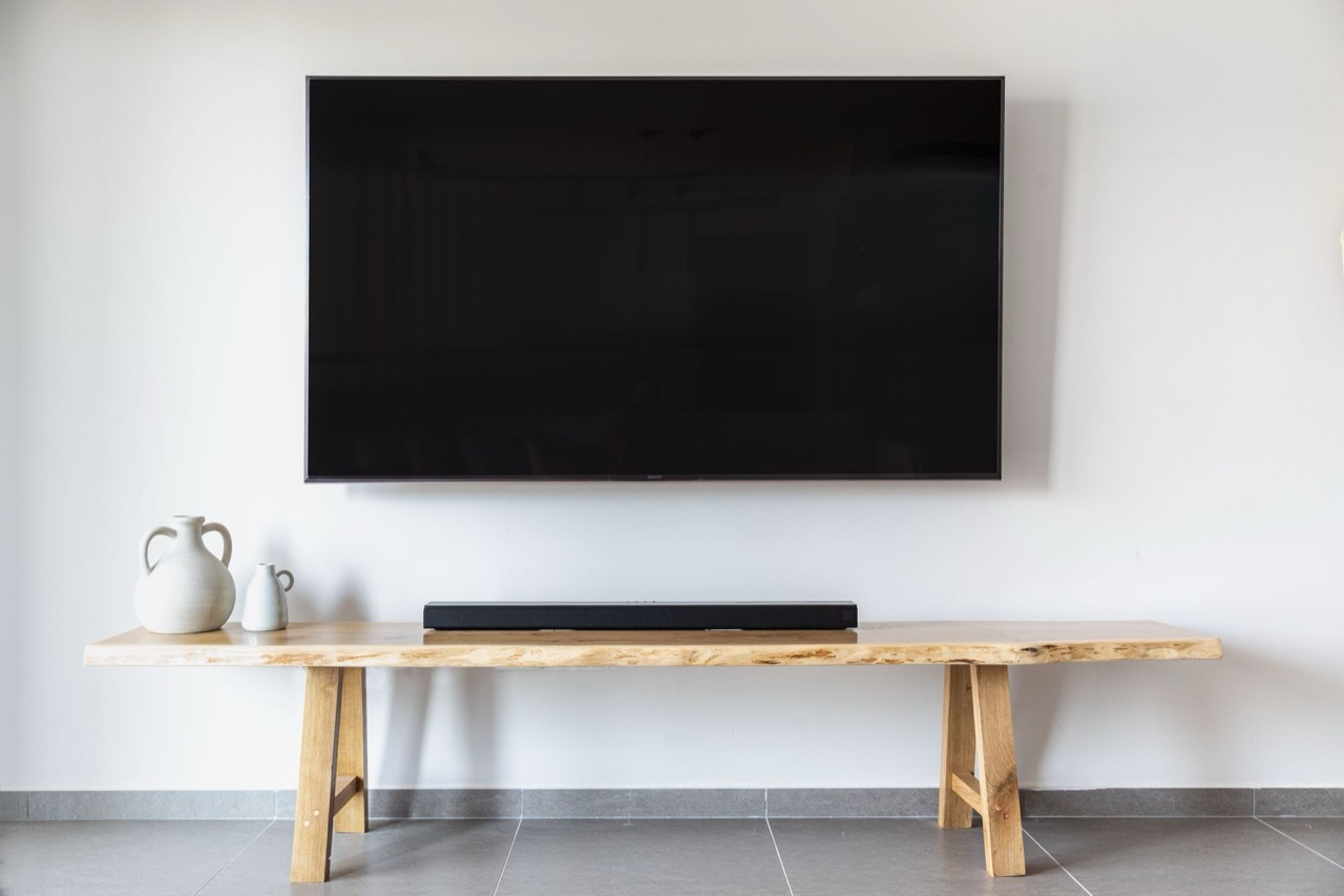 Wall-mounted television above a wooden console with a soundbar and white vases